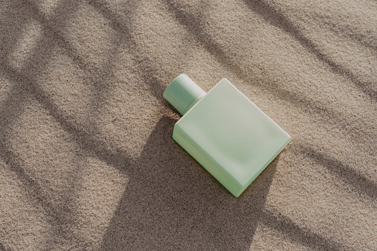 A minimalist perfume bottle lies elegantly on sand, casting soft shadows in natural light.